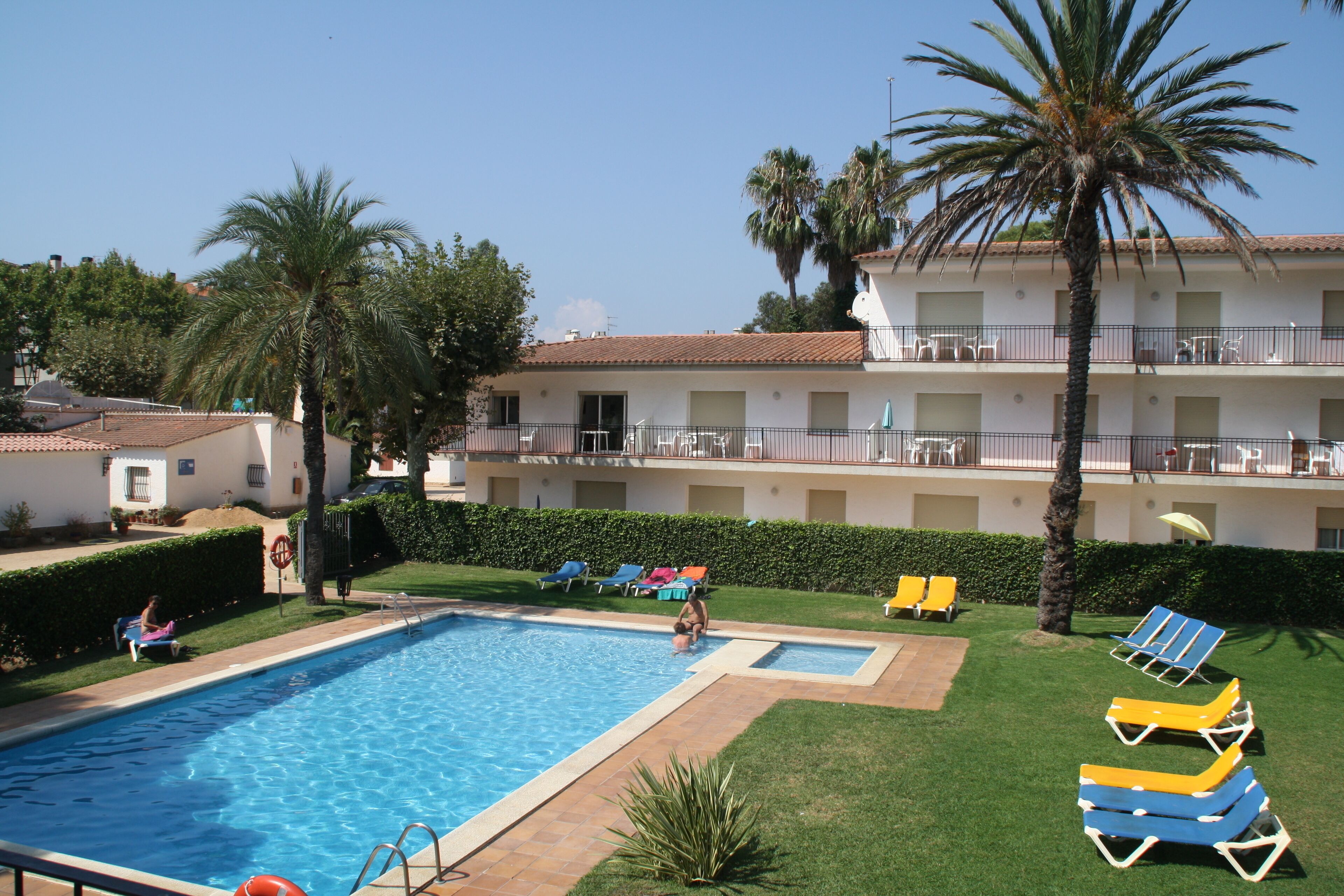 A swimming pool with lounge chairs, palm trees, and a building with balconies.