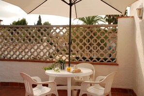 Eine Terrasse mit einem runden Tisch, zwei Stühlen, einem Blumentopf und einem Glas Orangensaft.