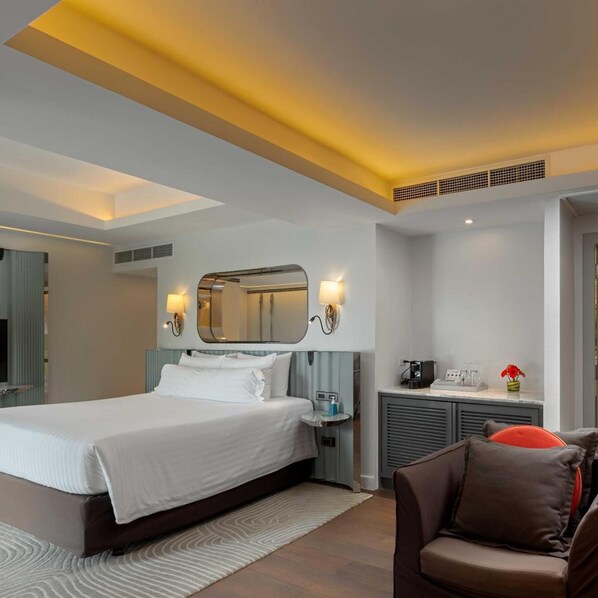 Une chambre d’hôtel moderne dotée d’un grand lit, de tables de chevet, d’un miroir, d’un petit coin salon et d’une kitchenette.