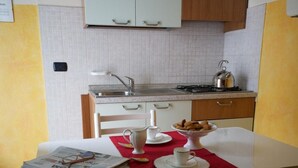 A dining area with a table set for two, a kitchen in the background, and a yellow wall. - Villa Terri (Verona)