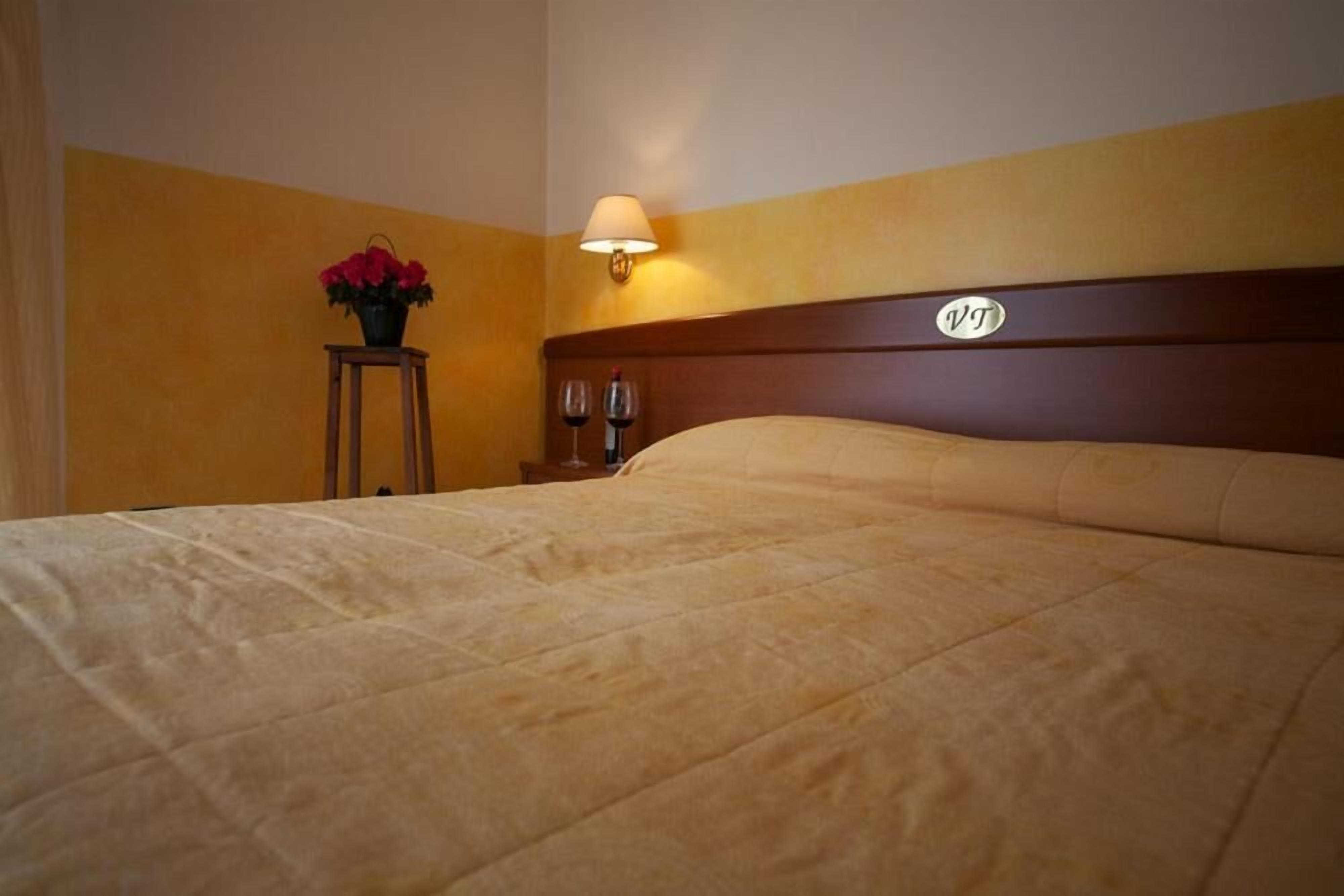 A hotel room with a bed, a nightstand with a lamp, and a sign on the headboard.