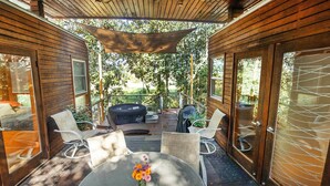 Un patio al aire libre cubierto con sillas de mimbre y una mesa, rodeado de paredes de madera y puertas de vidrio.