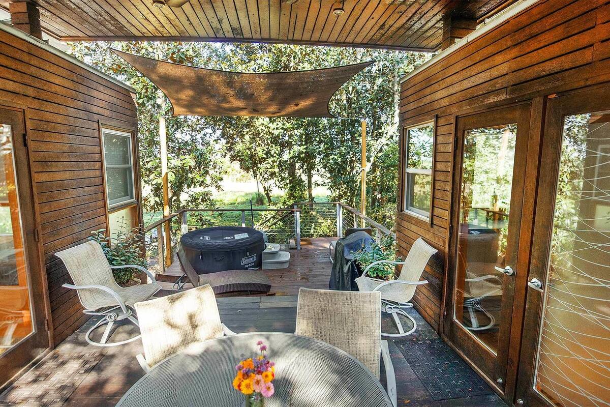 A covered outdoor patio with wicker chairs and a table, surrounded by wooden walls and glass doors.
