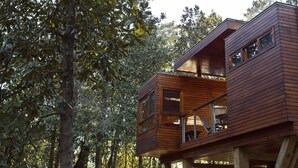 Una cabaña de madera con balcón y terraza en el segundo piso, rodeada de árboles.