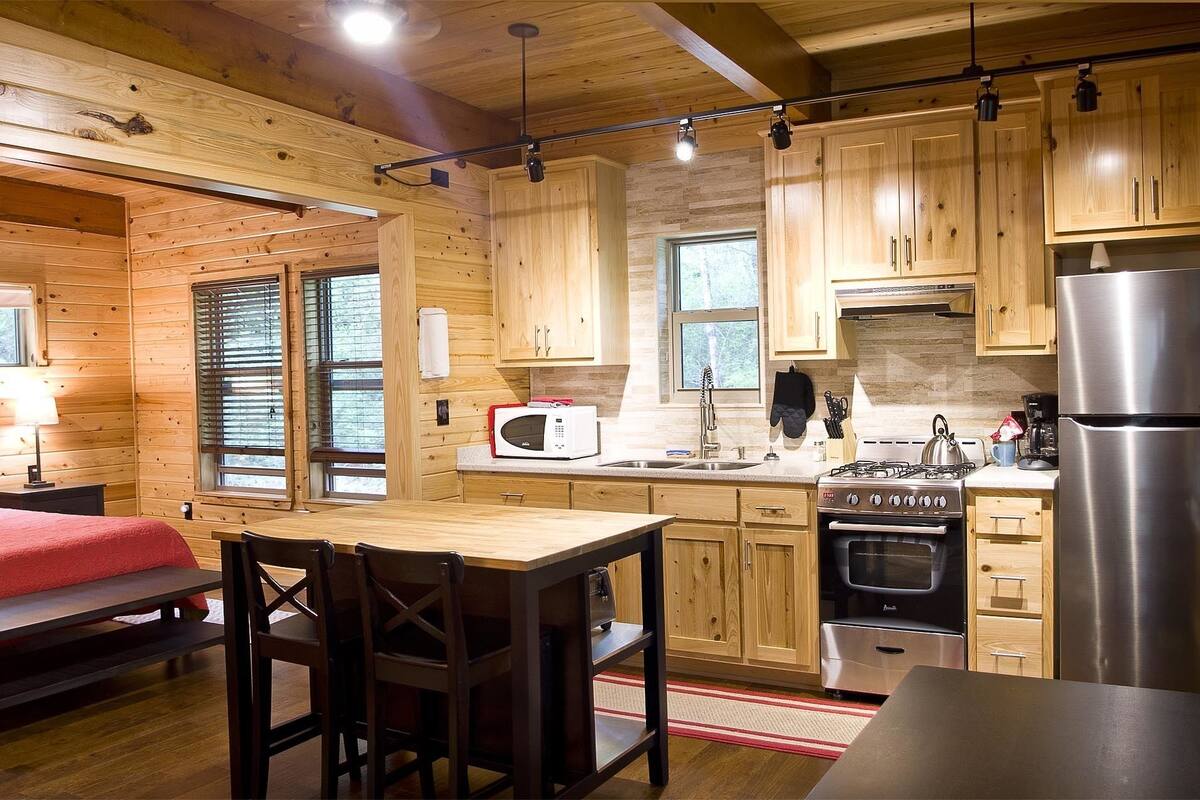 A cozy cabin-style room with a bed, a dining table, and a kitchenette.