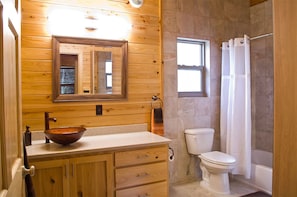 A wooden cabin bathroom with a wooden vanity, a large mirror, a vessel sink, a toilet, and a shower with a curtain.