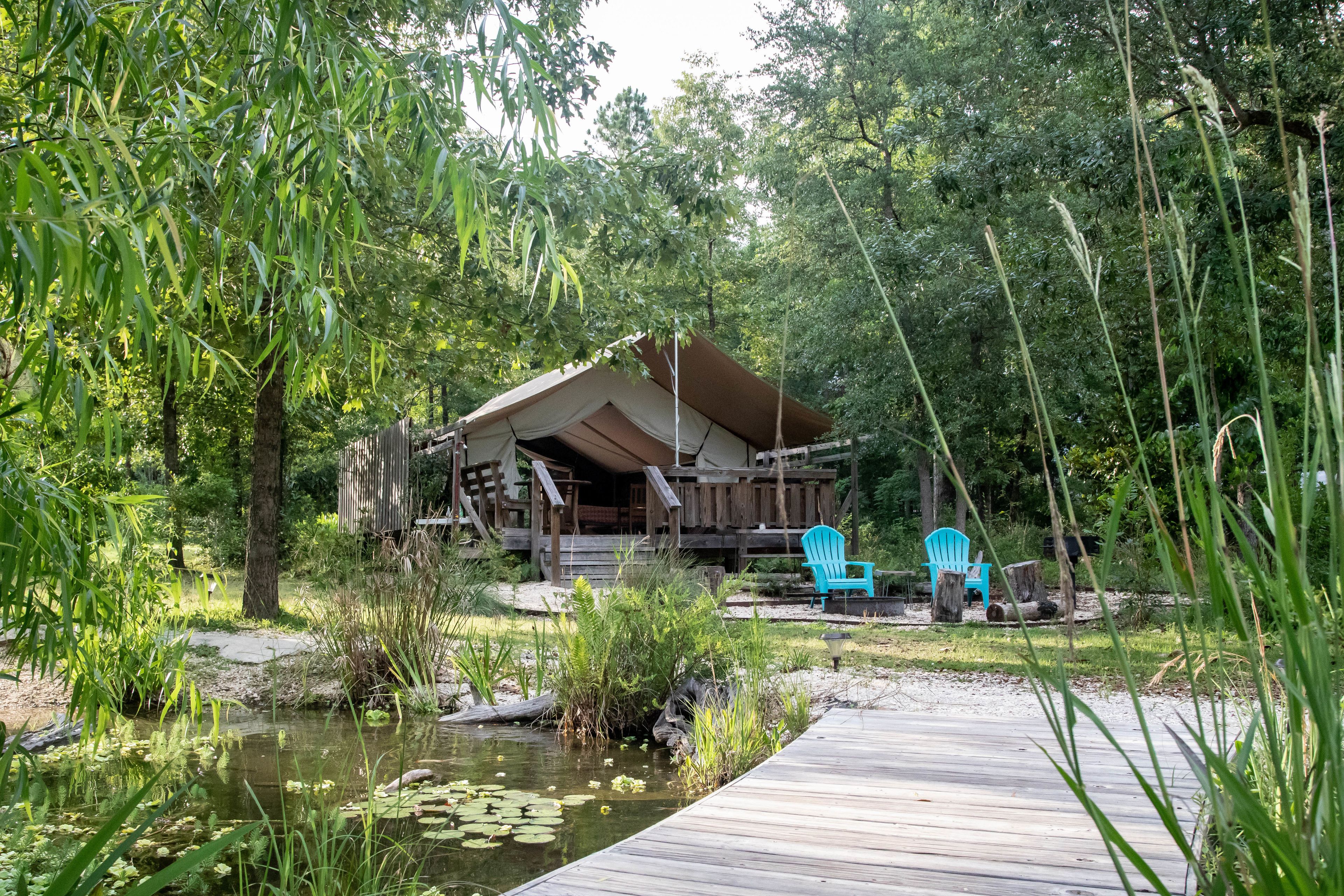 A rustic cabin with a wooden deck, surrounded by lush greenery and a small pond.