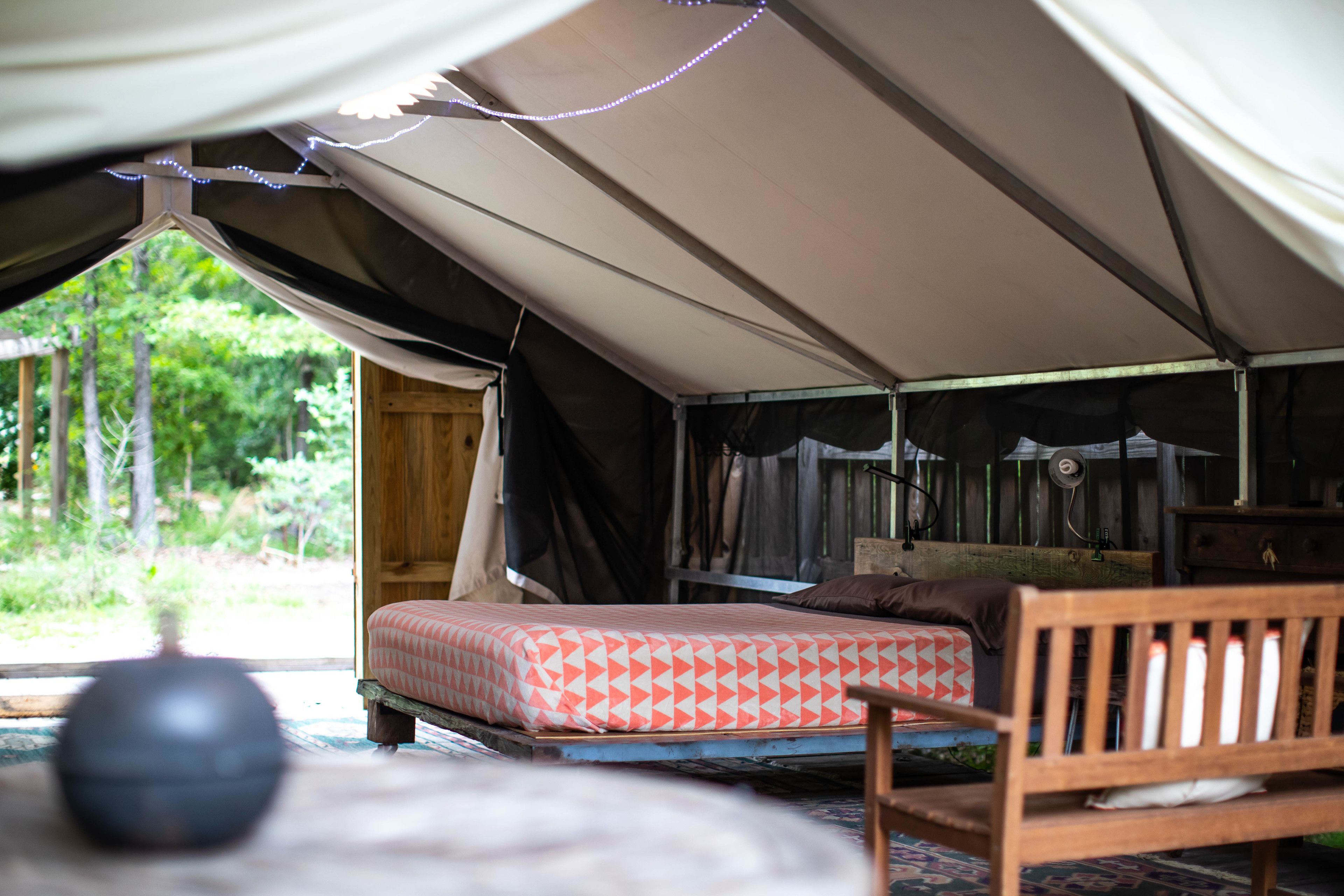 A tent with a bed, a wooden chair, and a small table.