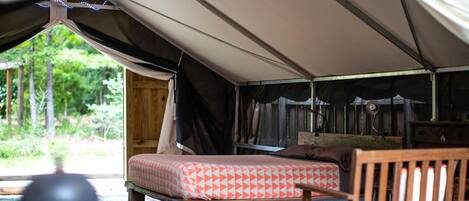 A tent with a bed, a wooden chair, and a small table.