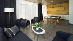 A modern living room with black sofas, a coffee table with a vase, and a dining area with wooden chairs and a white table. - Residence Trafick (Praha)
