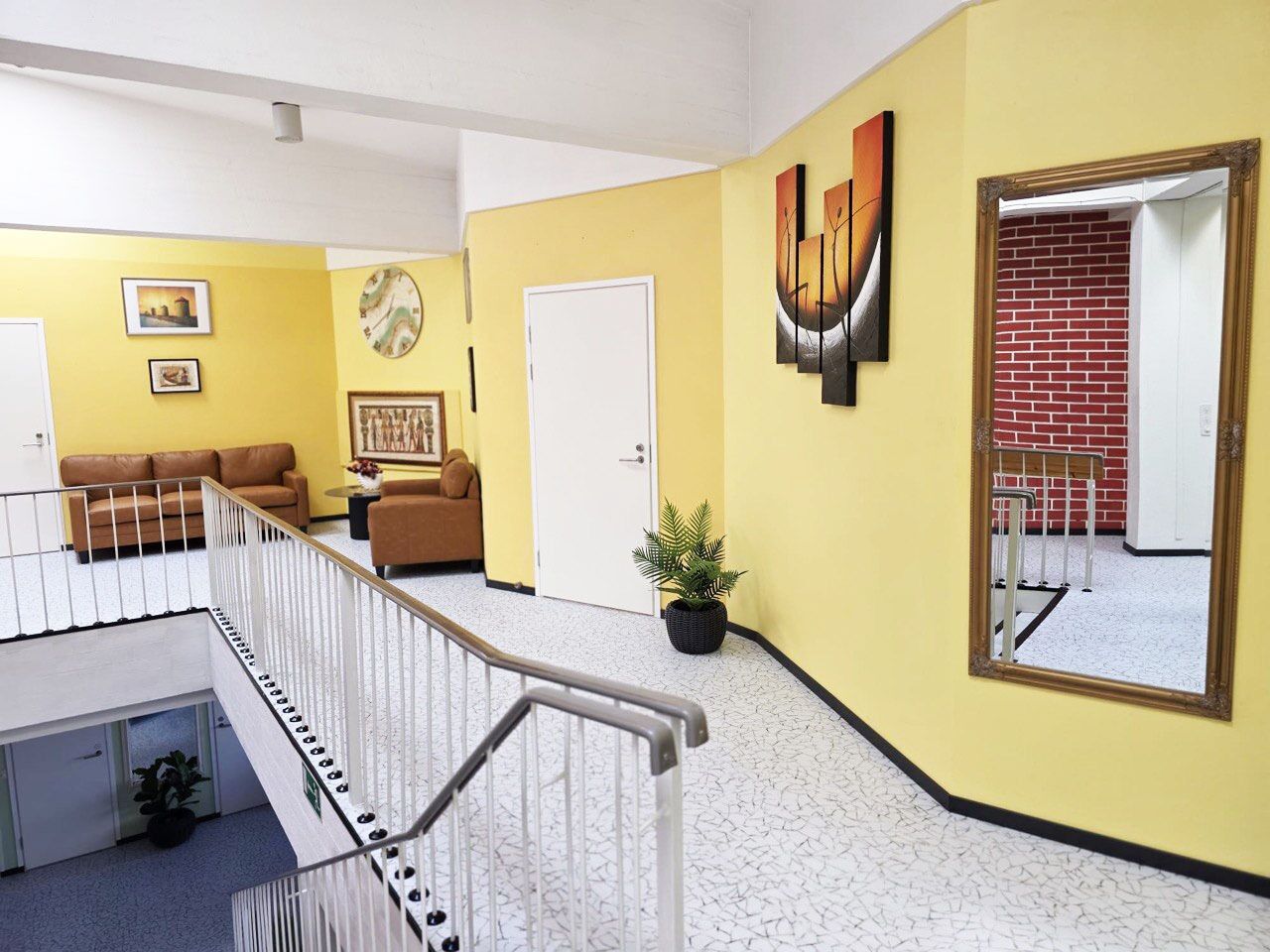 A hotel lobby with a staircase, yellow walls, a white door, and a large mirror.