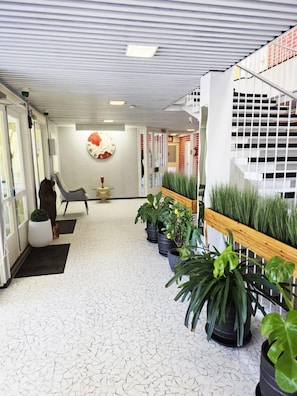 A corridor with a white tiled floor, potted plants, a bench, and a wall-mounted clock.