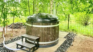 Una parrilla de madera al aire libre con un banco, rodeada por un borde de piedra y árboles.