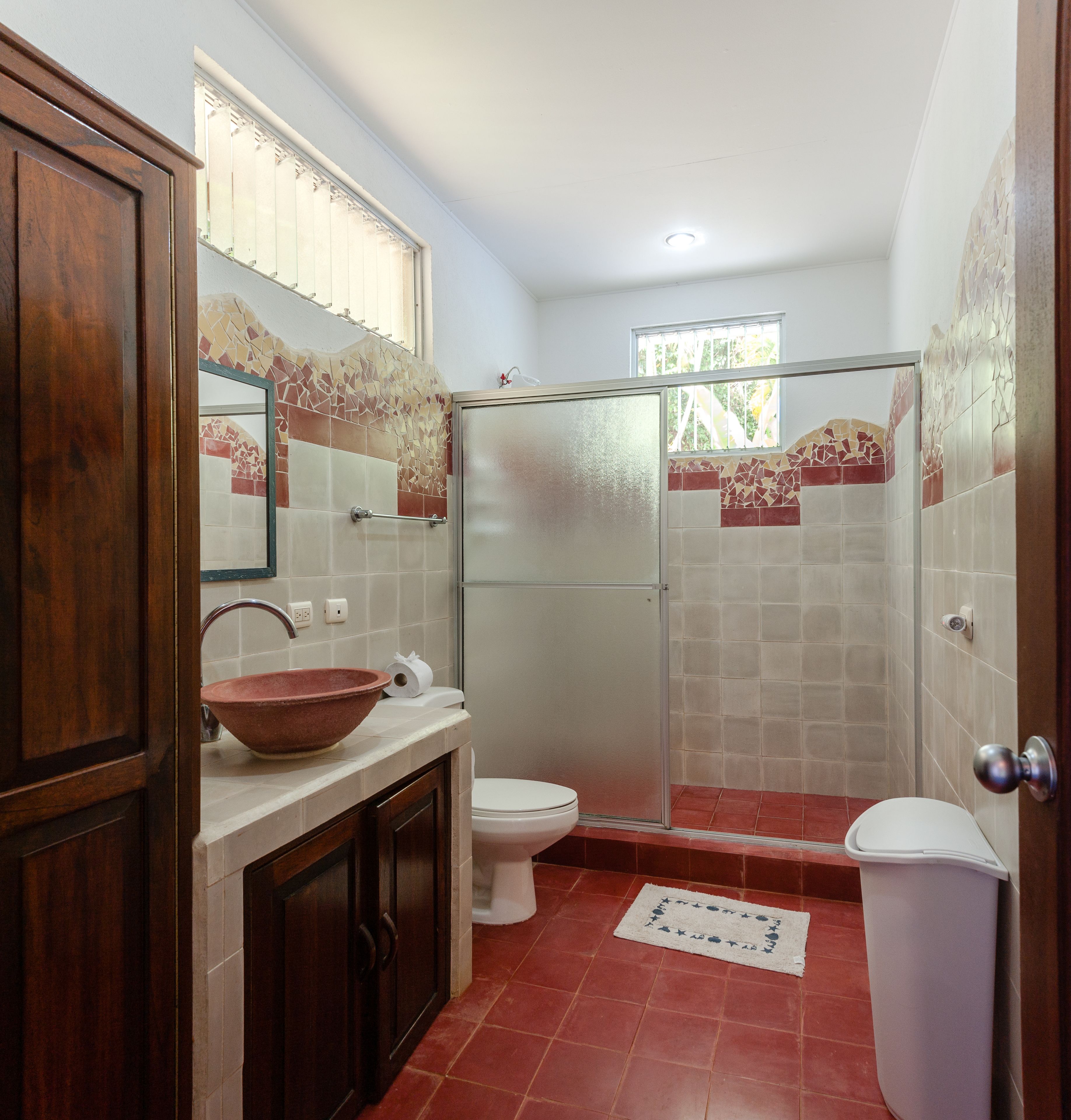 Une salle de bain avec un meuble en bois, un grand lavabo en forme de cuve, des toilettes et une cabine de douche en verre.