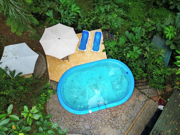 A small outdoor swimming pool with a tiled deck, surrounded by lush greenery.
