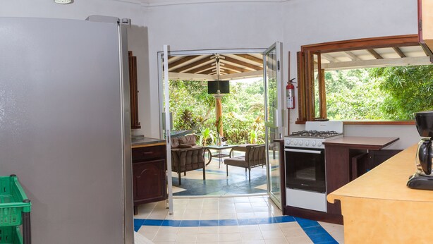 A kitchen with a stove, a dining area with a table and chairs, and a view of greenery outside. - Casa Cedro - Portasol Vacation Rentals (Savegre)