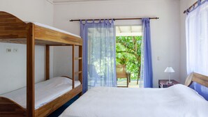 A room with a bunk bed, a single bed, a small table with a lamp, and a view of greenery outside. - Casa Cedro - Portasol Vacation Rentals (Savegre)