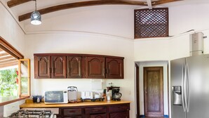 A kitchen with wooden cabinets, a gas stove, a refrigerator, and a microwave. - Casa Cedro - Portasol Vacation Rentals (Savegre)