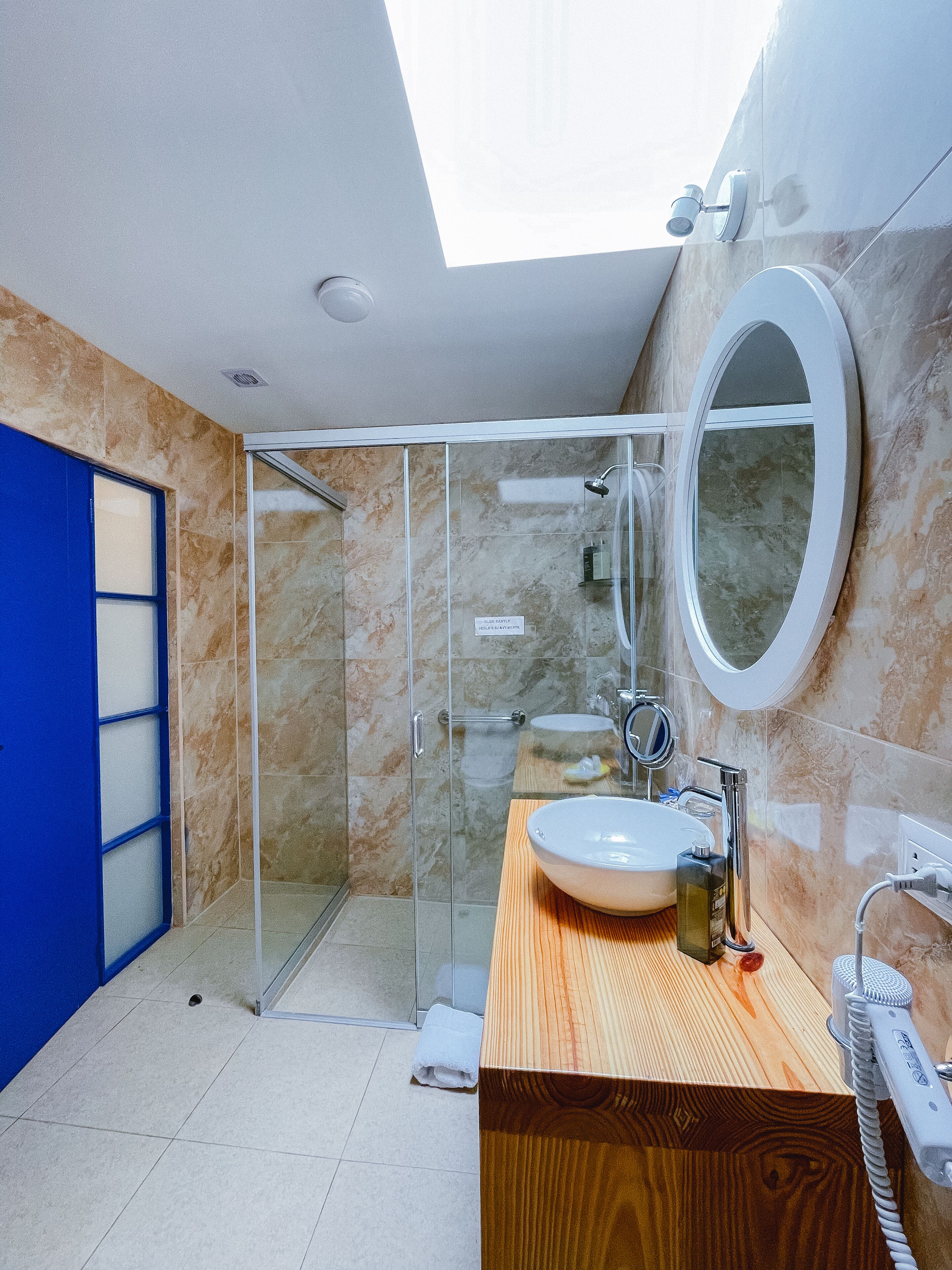 Un baño moderno con cabina de ducha de vidrio, tocador de madera, espejo grande y tragaluz.