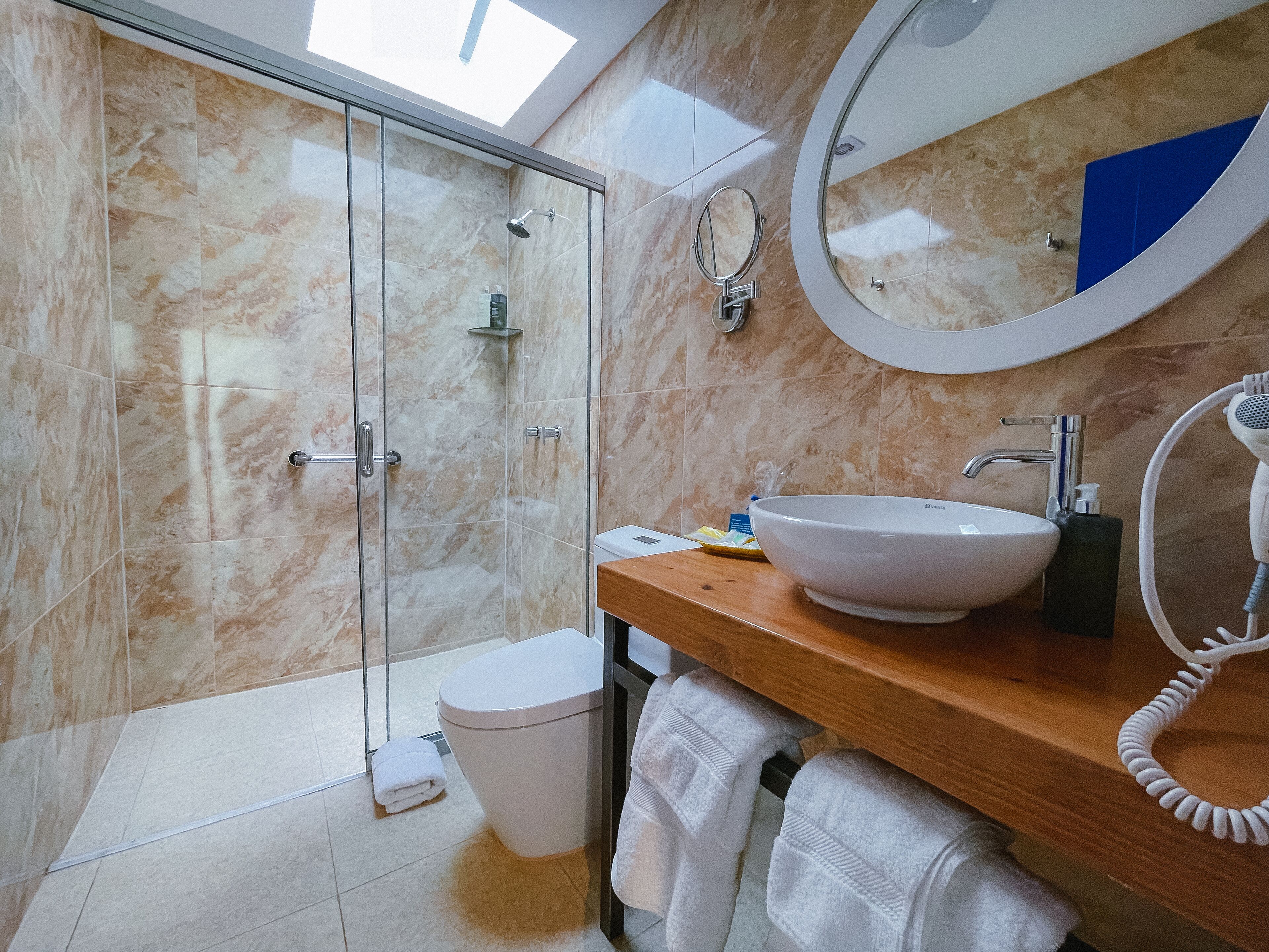 Un bagno moderno con doccia in vetro, lavandino bianco, specchio rotondo e porta asciugamani.