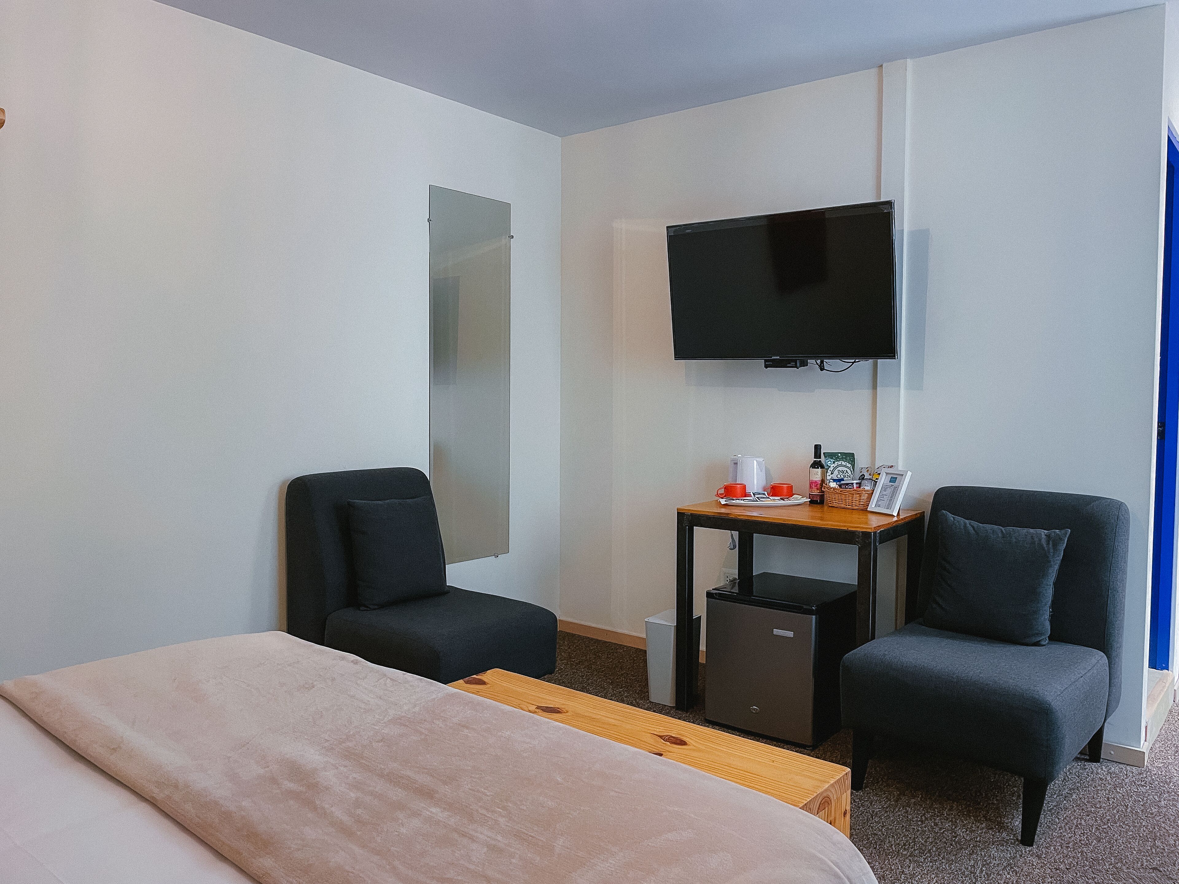 Habitación de hotel con cama, dos sillones, una mesita con cafetera, televisor y minibar.