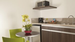 A compact kitchen with a microwave, coffee maker, and a small sink. There is a dining table with chairs and a vase with flowers. - San Simon Hotel Boutique (Pereira)