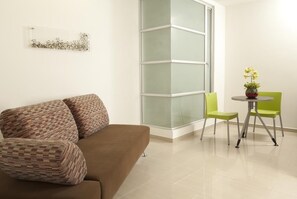 Ein modernes Wohnzimmer mit einem braunen Sofa, einer Glastrennwand, einem kleinen runden Tisch mit Stühlen und einer Vase mit Blumen.