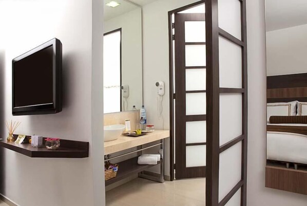 Una habitación de hotel moderna con televisor de pantalla plana, tocador con espejo, secador de pelo y cama con cabecera de madera.