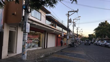 Uma rua com edifícios, carros estacionados e uma árvore.