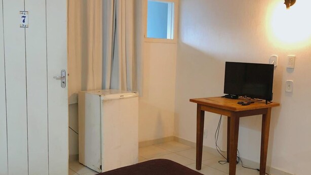 A hotel room with a bed, a desk with a television, a wardrobe, and a window with curtains. - Anexo Aldeia Buzios – Cama & Café (Búzios)