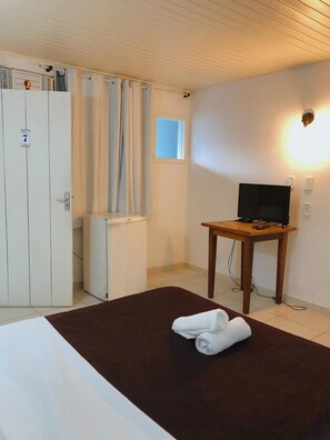 Habitación de hotel con cama, escritorio con televisor, armario y ventana con cortinas.