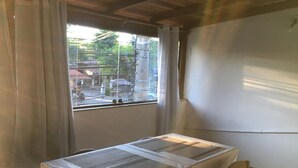 A room with a table and chairs, a window with curtains, and a view of the street outside. - Anexo Aldeia Buzios – Cama & Café (Búzios)