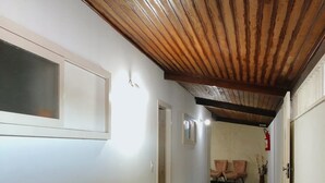 A hallway with wooden ceiling beams, white walls, and a dark floor. There are doors on the left and a vase on the right. - Anexo Aldeia Buzios – Cama & Café (Búzios)