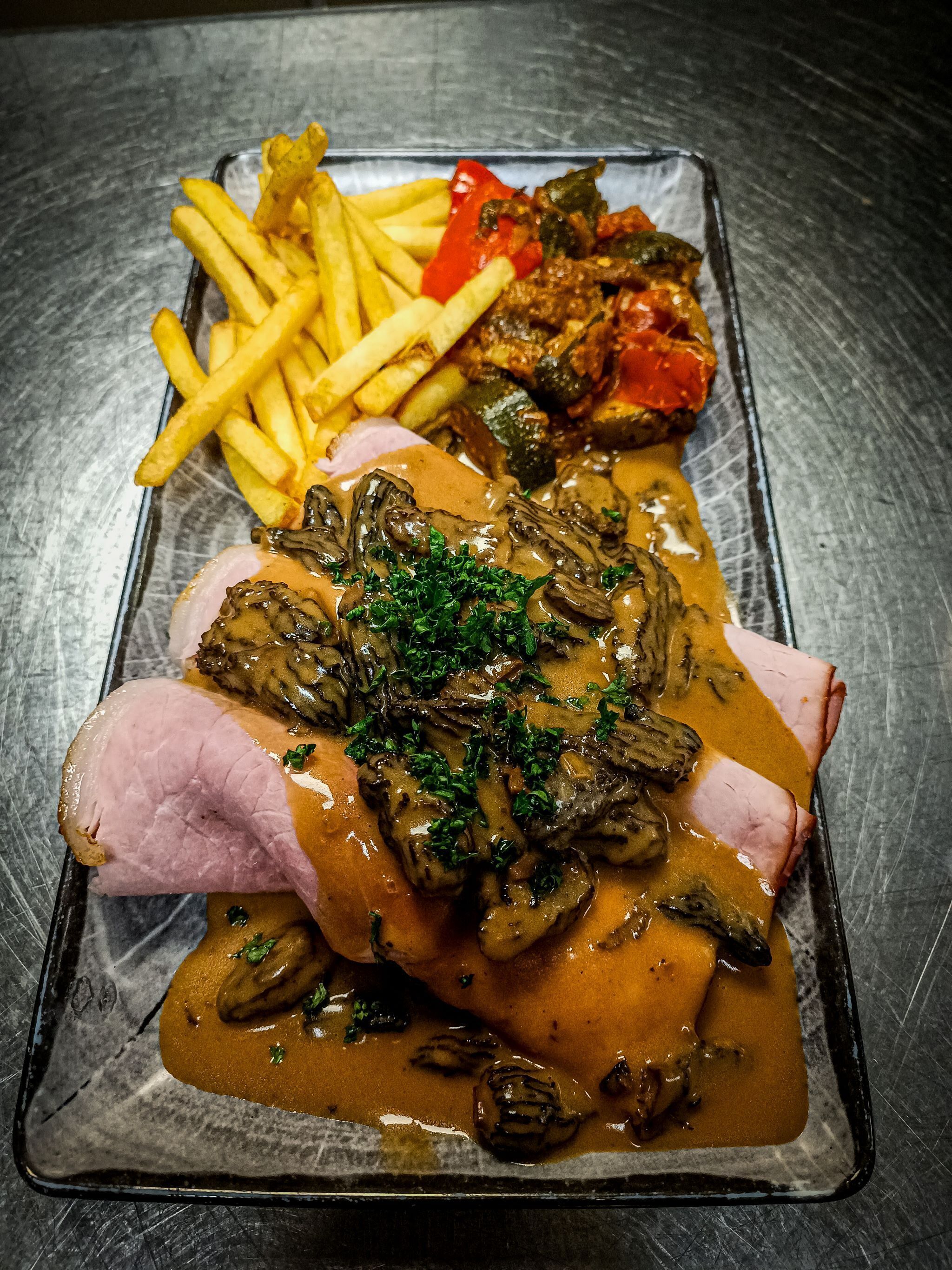 A plated meal with ham, mushrooms, and gravy, accompanied by French fries and vegetables.