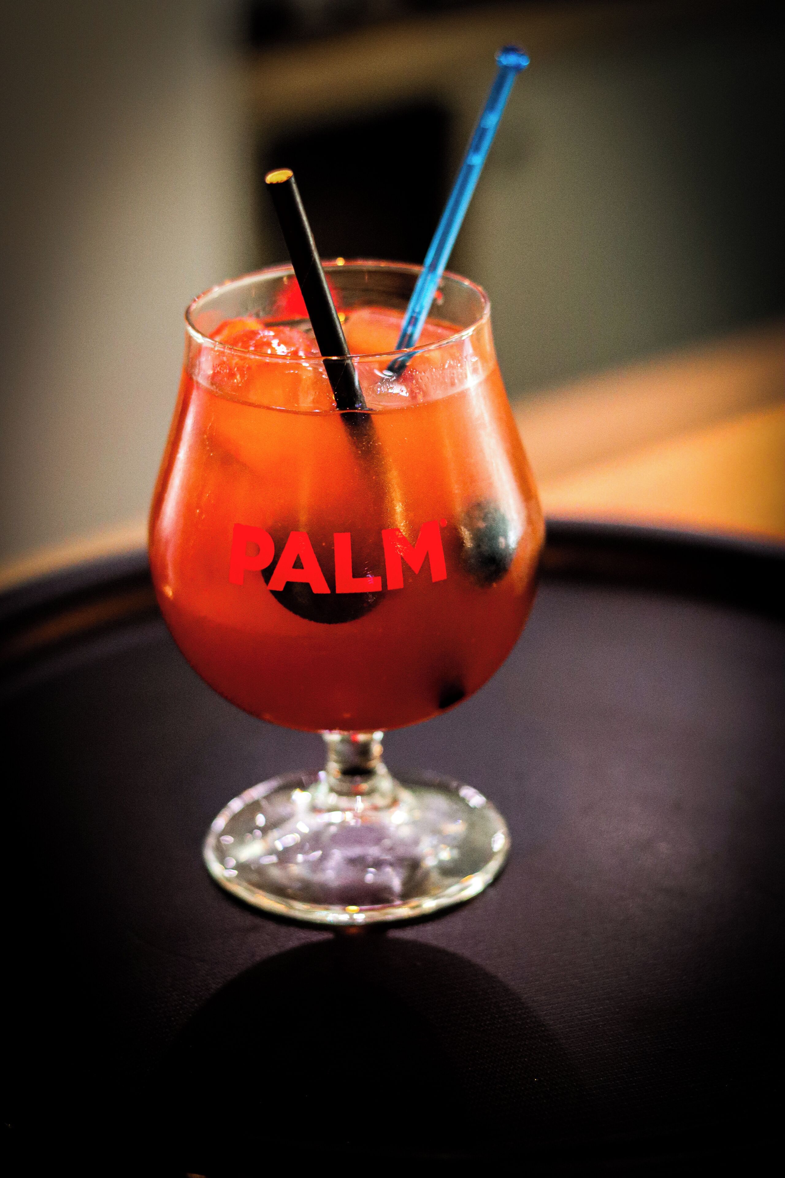 A glass with a red liquid and the word "PALM" on it, placed on a dark surface.