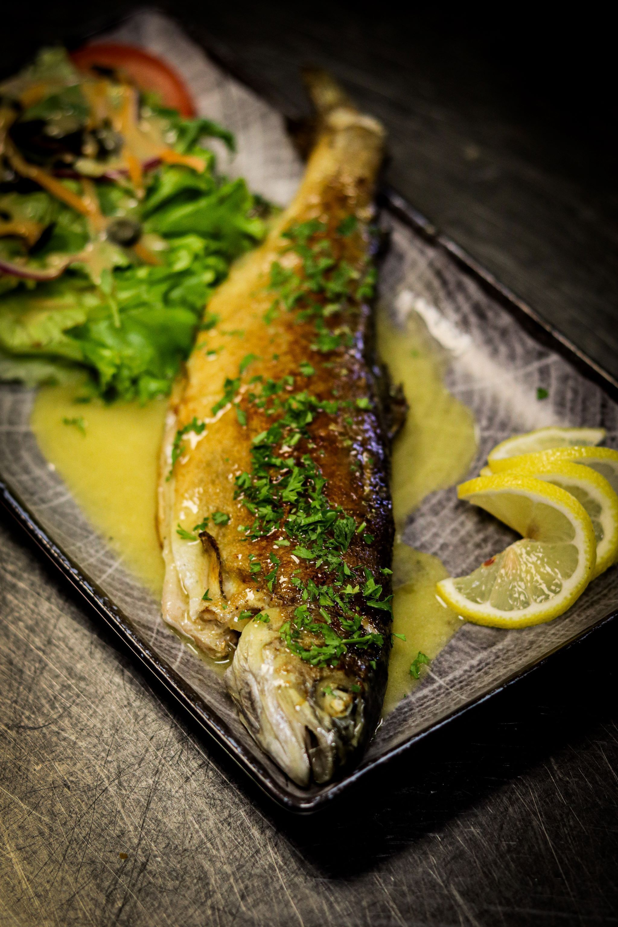 A whole roasted fish on a plate with lemon slices and a side salad.