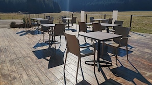 An outdoor dining area with tables and chairs on a wooden deck, overlooking a forested valley. - Auberge du Château de Joux (La Cluse-and-Mijoux)