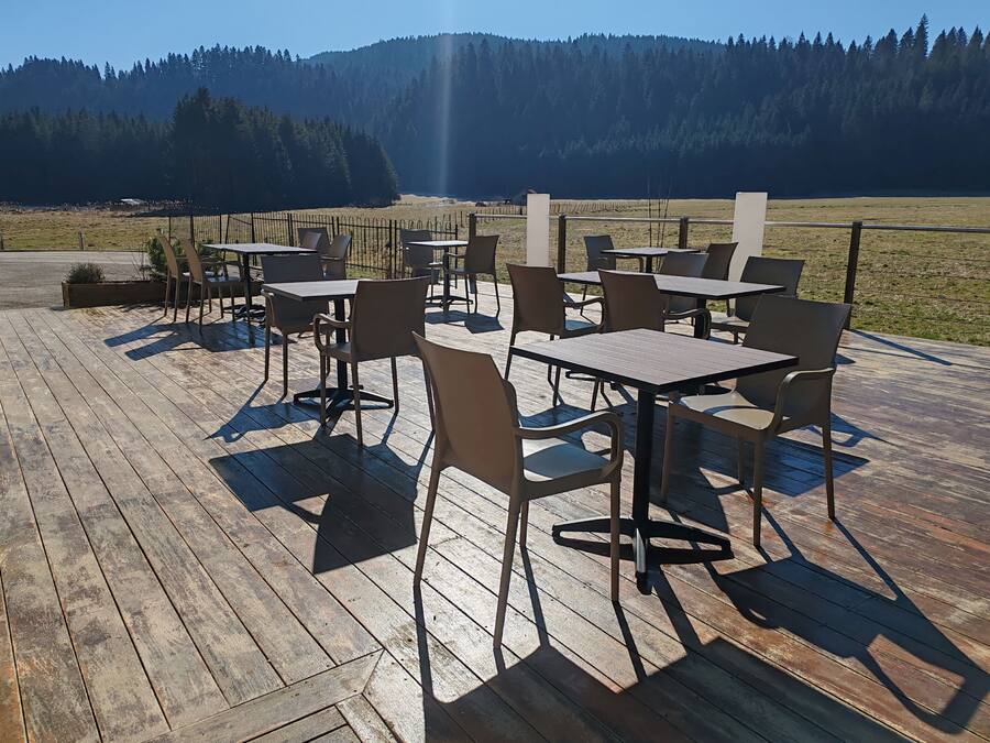 An outdoor dining area with tables and chairs on a wooden deck, overlooking a forested valley.
