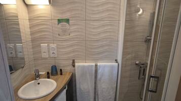 Ein modernes Badezimmer mit Waschbecken, Spiegel, Handtuchhalter und Duschkabine.