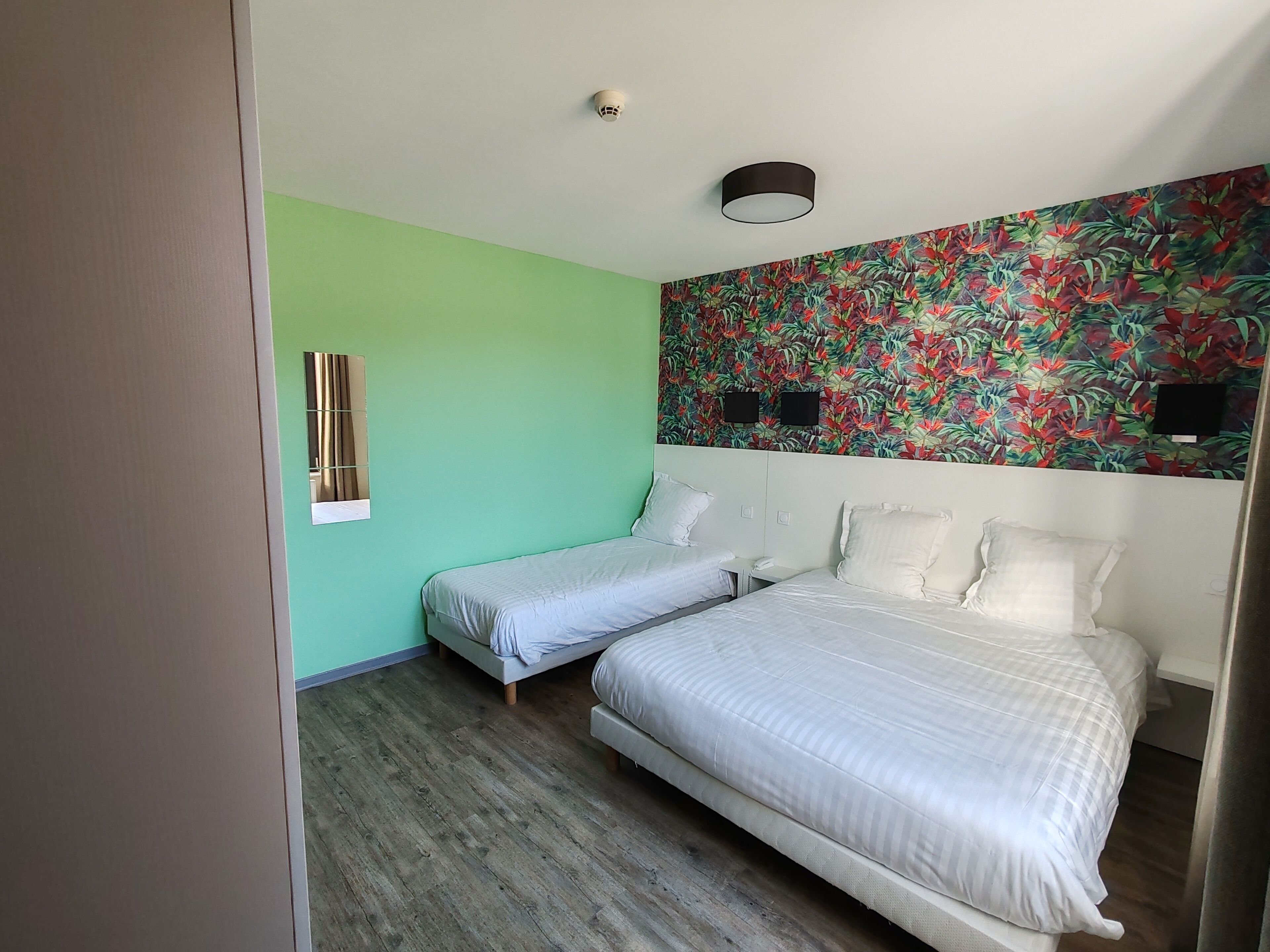 Una habitación con dos camas individuales, una cama grande, una pared verde, papel tapiz floral y suelo de madera.