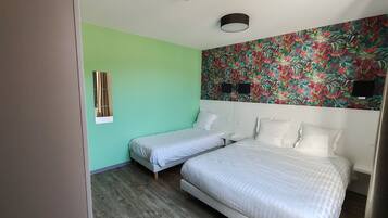 Una habitación con dos camas individuales, una cama grande, una pared verde, papel tapiz floral y suelo de madera.