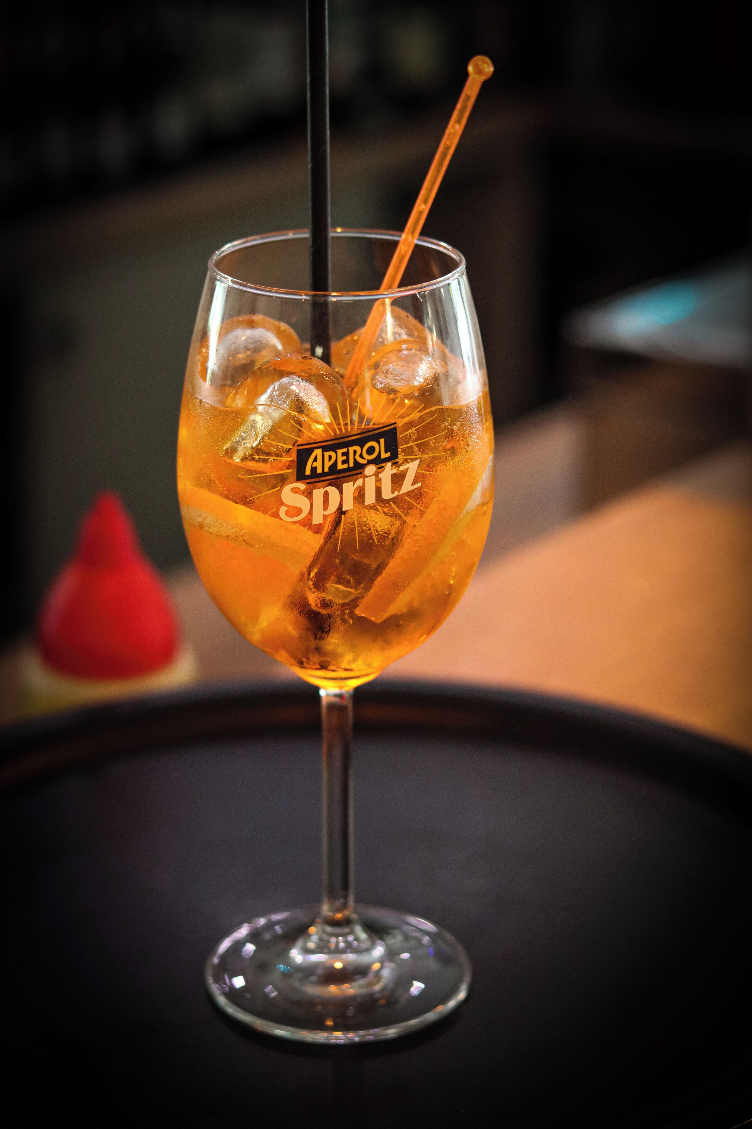 Et cocktailglas med sugerør, isterninger og en etiket med teksten "Aperol Spritz".