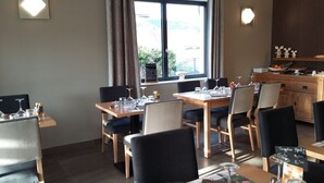 A dining area with tables set for two, chairs, and a view of the outdoors through a window. - Auberge du Château de Joux (La Cluse-and-Mijoux)