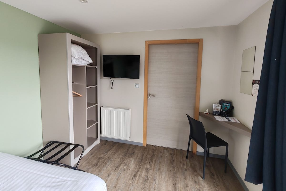 Habitación de hotel con cama, armario, escritorio con silla, televisor y radiador.