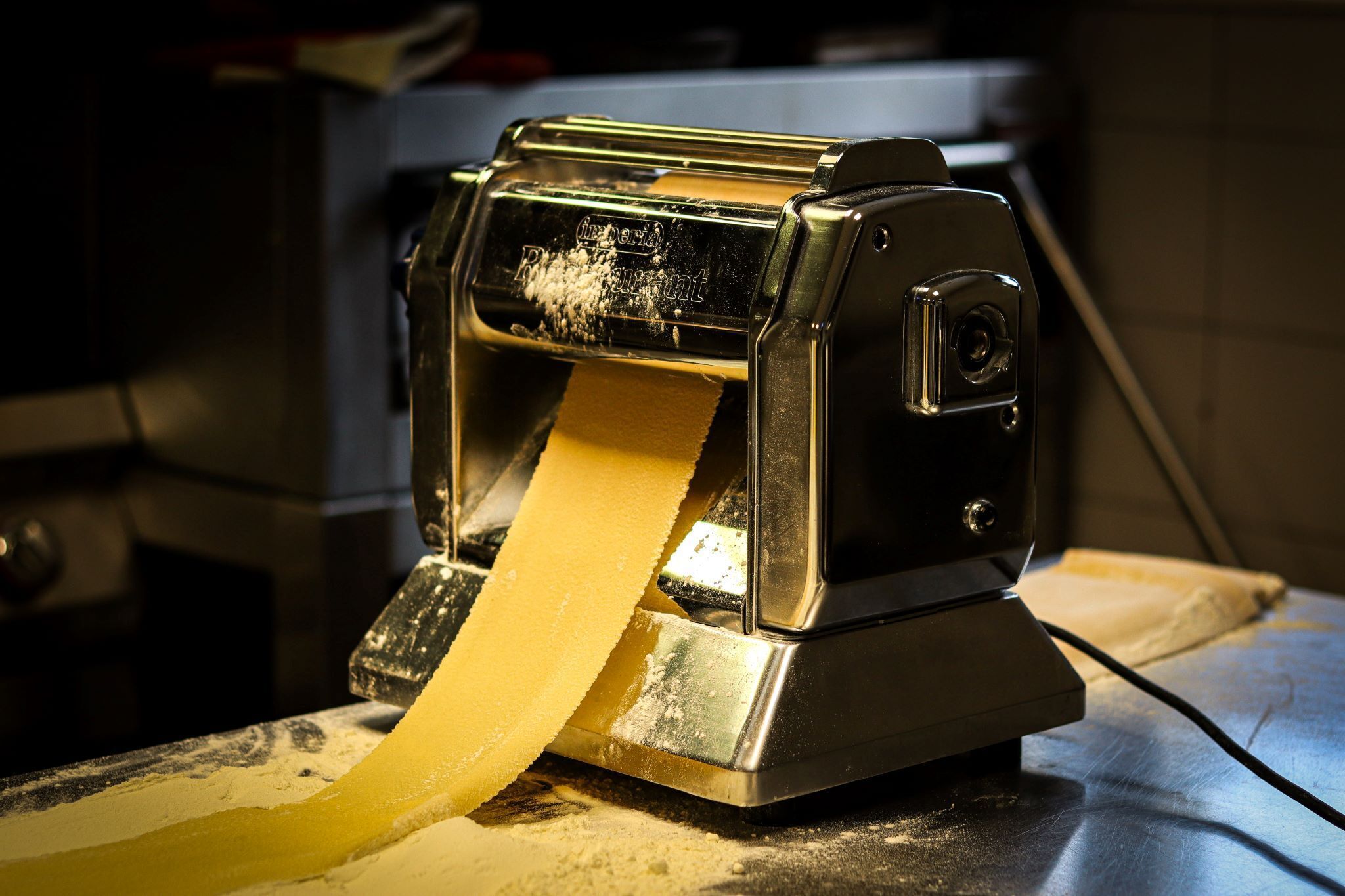 A pasta machine with a continuous pasta strip coming out of it.