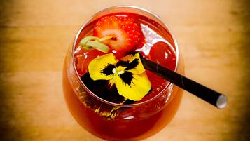 A glass with a red drink, a strawberry, and a yellow flower garnish on a wooden surface.