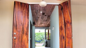A hallway with wooden doors leading to a room with a view of greenery outside. - Valley of Dreams Eco Lodge Room (Barú)