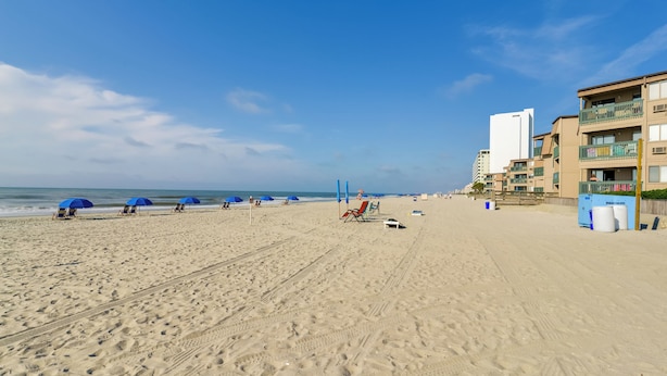 A beach with blue umbrellas, lounge chairs, and a building with balconies. - 2 Mi to Apache Pier: Gem w/ Pool Access (Myrtle Beach)