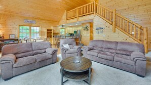 A spacious living room with two sofas and a coffee table, wooden walls, a staircase, and a kitchen area. - Lakefront Wisconsin Cabin with Boat Dock! (Birchwood)