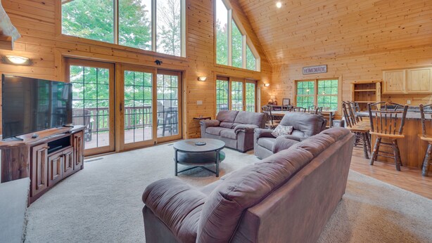 A spacious living room with a large sectional sofa, a flat-screen TV, and a dining area with wooden chairs and a table. - Lakefront Wisconsin Cabin with Boat Dock! (Birchwood)